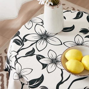 Round cotton linen tablecloth with black floral patterns and tassel edges on a table