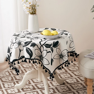 Close-up of cotton linen tablecloth featuring black floral prints and elegant tassels