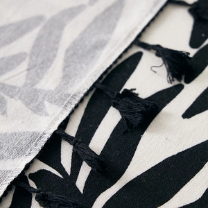 Close-up of tropical leaf print on linen tablecloth with black tassel fringe detail