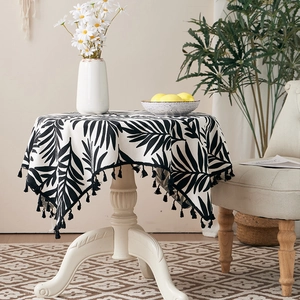 Detailed view of round cotton linen tablecloth with black and white leaf prints and fringe
