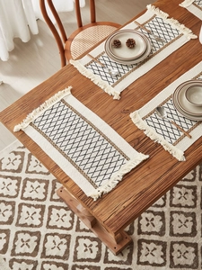 Close-up of diamond pattern woven placemat with fringed edges on wooden table