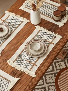 Detail of bohemian rectangle placemat with black diamond patterns and fringe on wood table