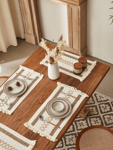 Detailed macro view of beige woven table runners with fringe on a wooden table setup