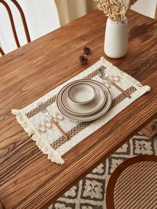 Macro detail of bohemian woven table runner with tassels and ceramic tableware on wood