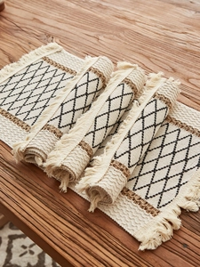 Detail of woven table runner with diamond patterns and long tassels on wooden table