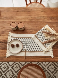 Close-up of bohemian linen placemat with black diamond patterns and handmade tassels