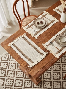 Close-up of woven cotton placemats with brown stripes and tassels on a wooden dining table