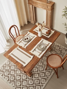 Bohemian off-white table mats with woven brown stripes and fringe tassels on a wooden table