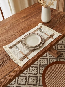 Detail of woven table runner with brown stripes and fringe on a wooden table