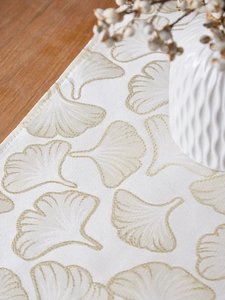 Detail of elegant white table runner featuring gold ginkgo leaf embroidery texture