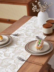 Close-up of golden ginkgo leaf embroidery on beige linen table runner fabric