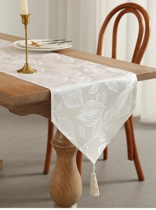 Detailed embroidery of leaf patterns on luxury ivory table runner with tassel accent