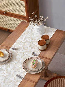 Detail of golden ginkgo leaf patterns on a cream textured table runner fabric