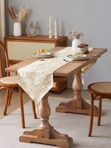 Detail of cream jacquard table runner with gold floral embroidery and white fringe tassels