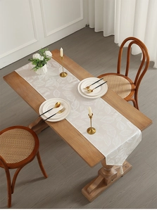Close-up of cream table runner with leaf pattern and elegant tassel on a wooden table