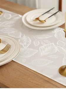 Gros plan du chemin de table crème avec broderie de feuilles et texture satinée