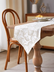 Detail of gingko leaf embroidery on table runner with tassel on dark wooden table