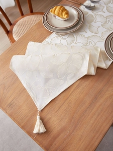 Detailed view of beige ginkgo leaf jacquard table runner with decorative tassel trim