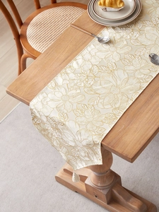 Close-up of golden floral embroidery and tassel detail on luxury cream table runner