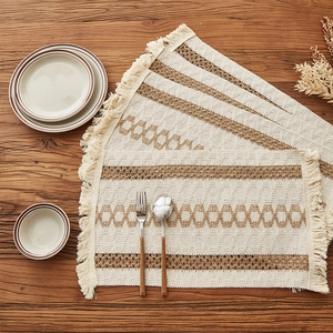 Woven tassel placemat with cream and brown geometric patterns on a dark wood table