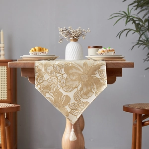 Elegant beige and gold jacquard floral table runner with tassels on wood dining table
