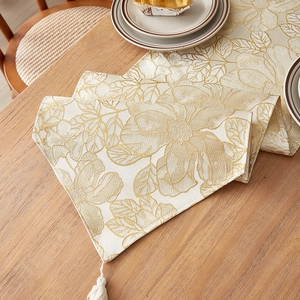 Luxury beige table runner with gold floral embroidery and tassel on wooden table