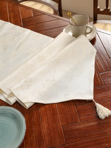 Detail van de crème tafelloper met jacquard bloemenpatroon en elegante franje kwastjes