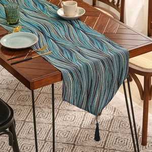 Modern wavy table runner with blue jacquard fabric and luxury silk tassels on dark wood
