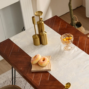 Luxe crèmekleurige jacquard tafelloper met bloemenpatroon op een donkere houten tafel
