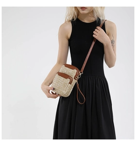 Model wearing a straw woven crossbody phone bag with brown leather trim and zip pockets