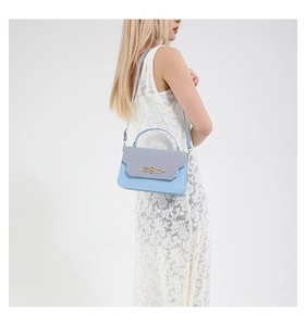 Detail of light blue crossbody bag with woven grey flap and golden metal lock buckle