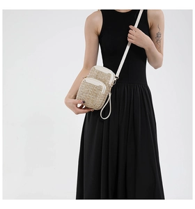 Detail of dual zipper compartments and white leather trim on a woven straw crossbody bag