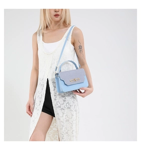 Detail of light blue crossbody bag featuring a golden lock and textured flap detail