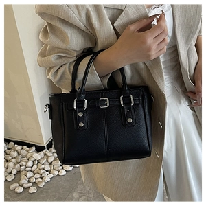 Close-up of black lychee-grain leather tote bag with silver buckles on fashion model