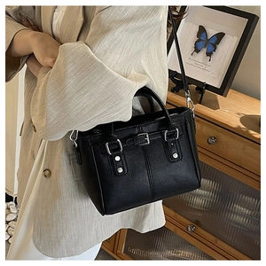 Detail of black pebbled leather tote bag with silver studs and buckles worn over a beige suit