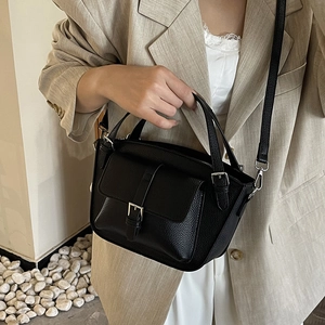 Classic black bucket bag in pebble leather worn by model with beige blazer suit