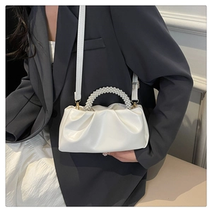 Detail of white pleated cloud bag with pearl handle worn by model in gray blazer