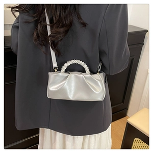 Close-up of silver pleated cloud bag featuring pearl handle and leather crossbody strap