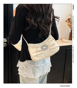 Close-up of pleated cream underarm bag featuring a centered rhinestone decorative buckle