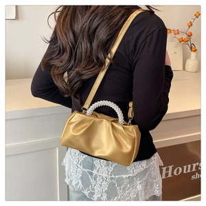 Sac nuage doré plissé avec poignée en perles porté par un mannequin dans un décor