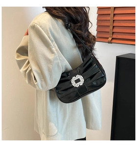 Detail of black patent leather bag featuring a large crystal buckle and pleated texture