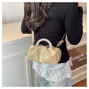 Detail of cream pleated cloud bag with pearl handle and adjustable shoulder strap on model