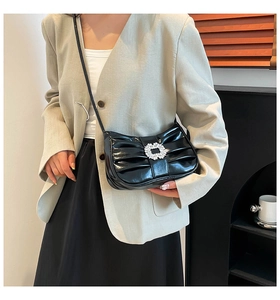 Detailed view of black patent leather crossbody bag with pleated texture and crystal buckle