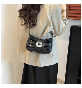 Detail of black pleated shoulder bag with rhinestone buckle worn by a model