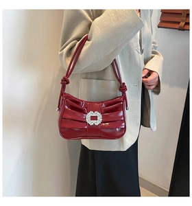 Detailed view of dark red patent leather bag featuring elegant pleated design and crystal buckle