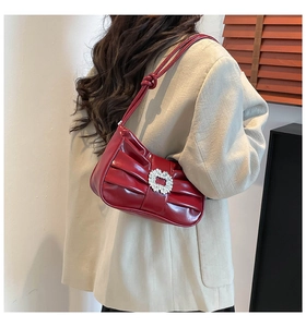 Detail of red pleated shoulder bag with rhinestone buckle worn over a beige blazer