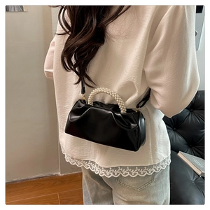 Detail of black pleated cloud bag with pearl handle and golden hardware on shoulder