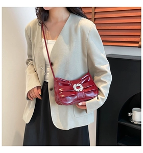 Close-up of wine red patent leather bag with pleated bow design and rhinestone buckle