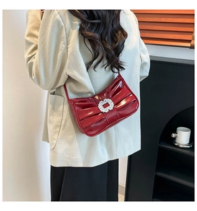Detail of red patent leather shoulder bag with pleated bow design and rhinestone buckle