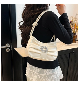 Detail view of white pleated shoulder bag with large rhinestone buckle and knotted strap